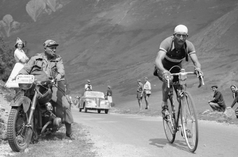 Gino Bartali pedaleando en su bicicleta por una carretera, en una fotografía en blanco y negro tomada durante la década de 1940.