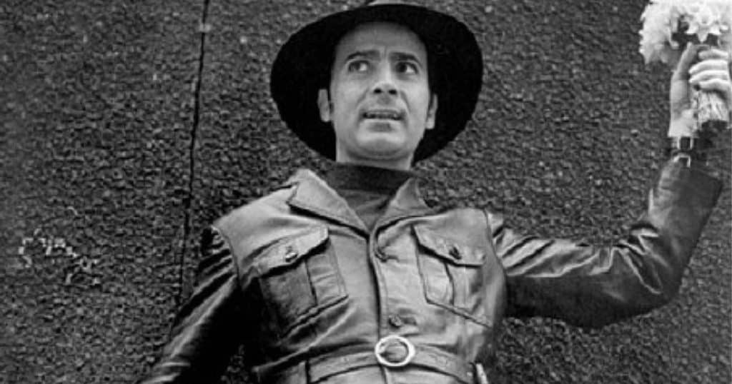 Manuel Puig con sombrero y chaqueta de cuero sosteniendo un ramo de flores