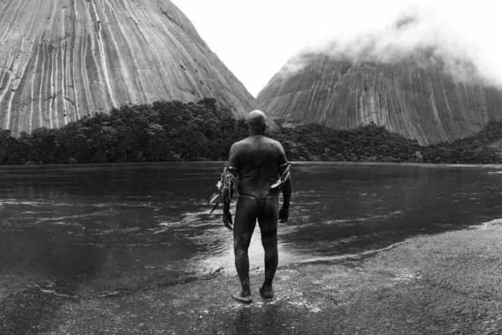 Fotograma de El abrazo de la serpiente, de Ciro Guerra. Río, selva y personaje de espaldas. Blanco y negro. Un clásico entre las películas colombianas del siglo XXI