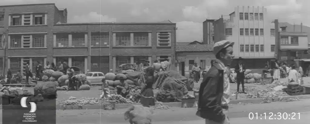Fotograma de Raíces de piedra, de José María Arzuaga, con una escena urbana de trabajo popular en Bogotá.