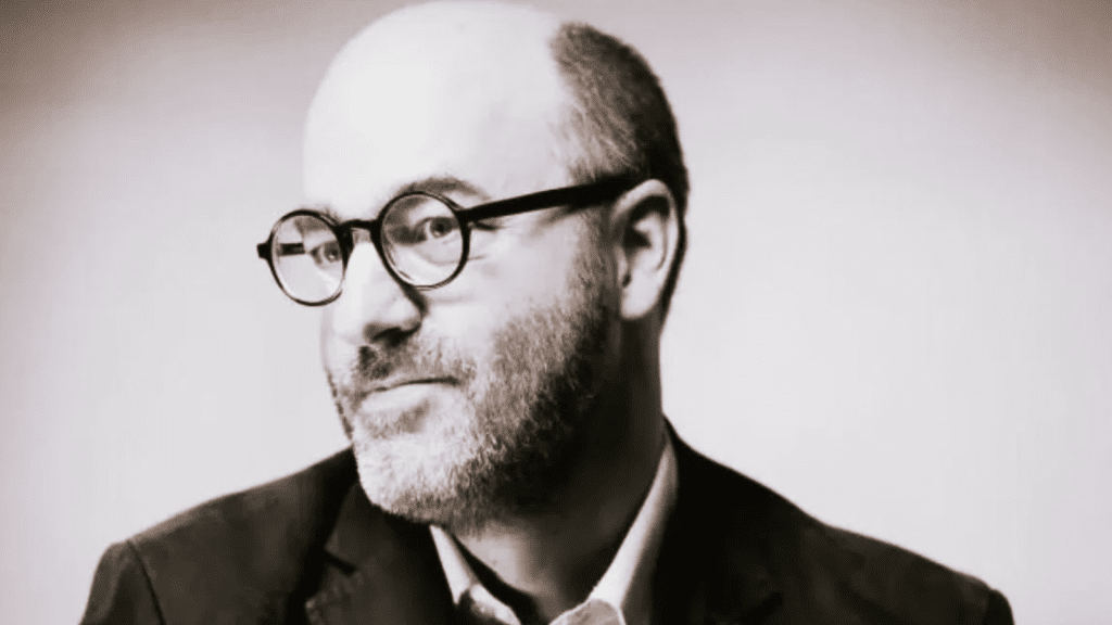 Alain Deneault, filósofo canadiense, autor de Mediocracia, en retrato con gafas redondas y traje oscuro