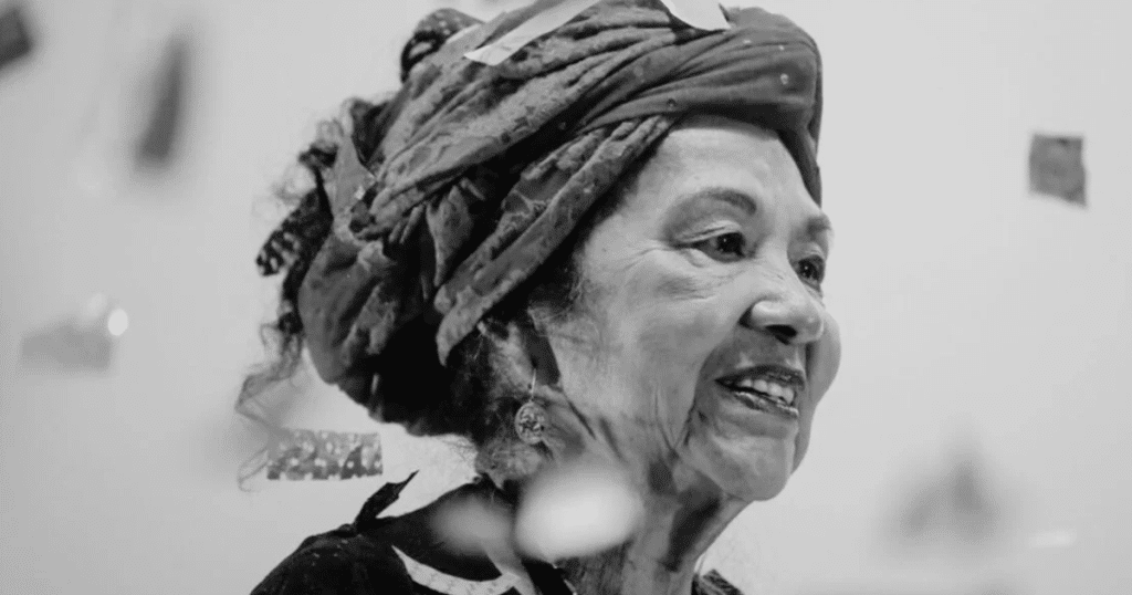 Retrato en blanco y negro de Totó la Momposina sonriendo, con turbante tradicional y mirada hacia un costado, en una imagen sobria y documental.