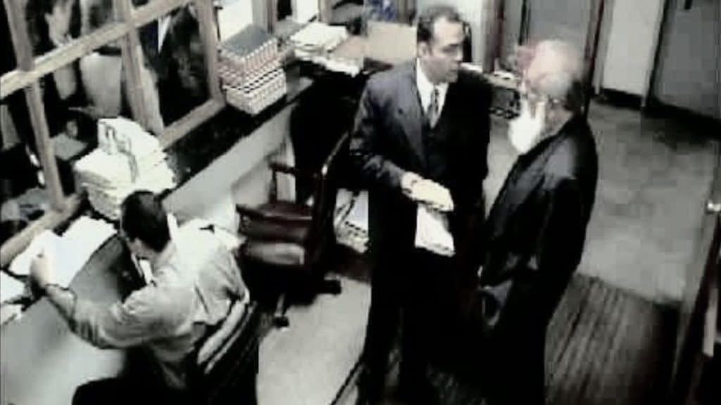 Escena en blanco y negro de La pena máxima en una oficina, con Mariano Concha hablando con un hombre mayor mientras un empleado trabaja entre papeles y archivos.