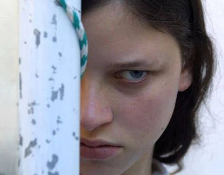 Escena de La niña santa, de Lucrecia Martel, con una joven observando desde detrás de una estructura.