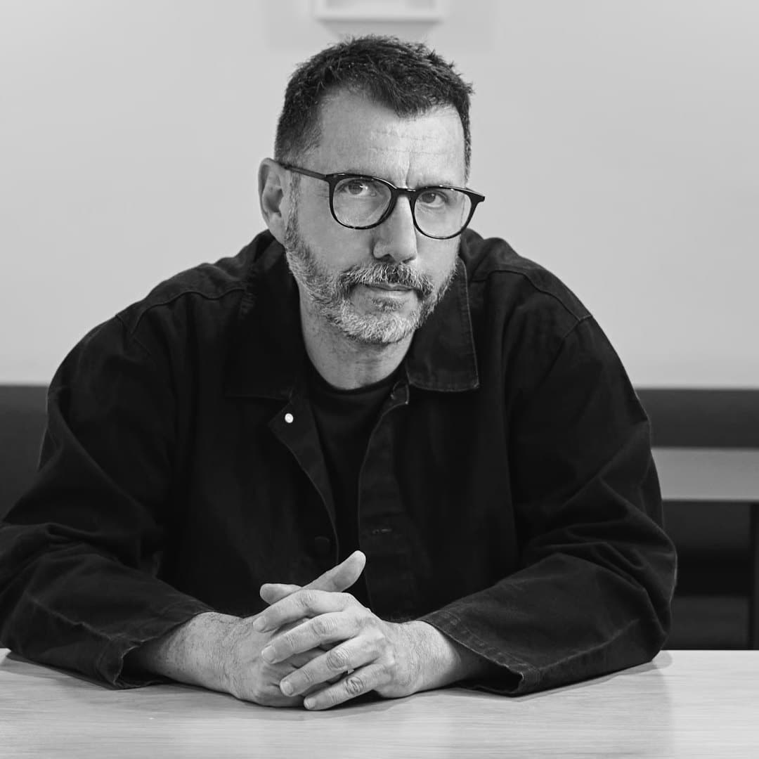 Retrato en blanco y negro de Alberto Fuguet, con gafas y barba, sentado con las manos entrelazadas sobre una mesa