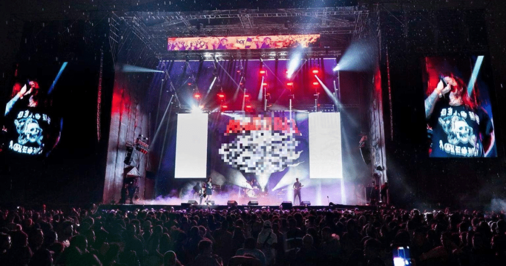Vista panorámica de un concierto de Rock al Parque en Bogotá, con una multitud frente al escenario iluminado y dos pantallas gigantes que muestran al cantante.